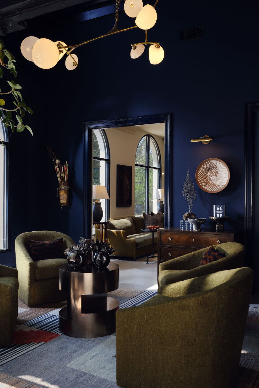 Luxurious living room with dark blue walls, green chairs, and a chandelier.